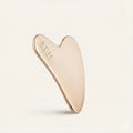 Rose gold gua sha tool with 'RUH' branding on a light beige background