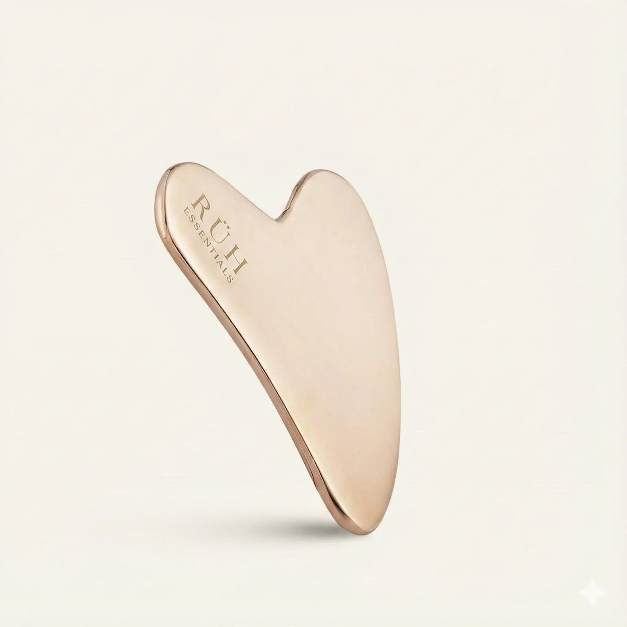 Rose gold gua sha tool with 'RUH' branding on a light beige background